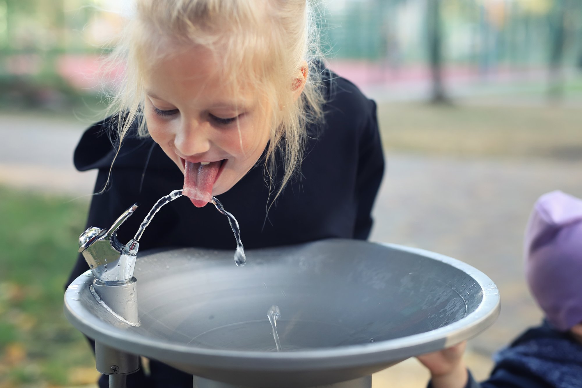 a young girl drinking out of a water fountain outside 