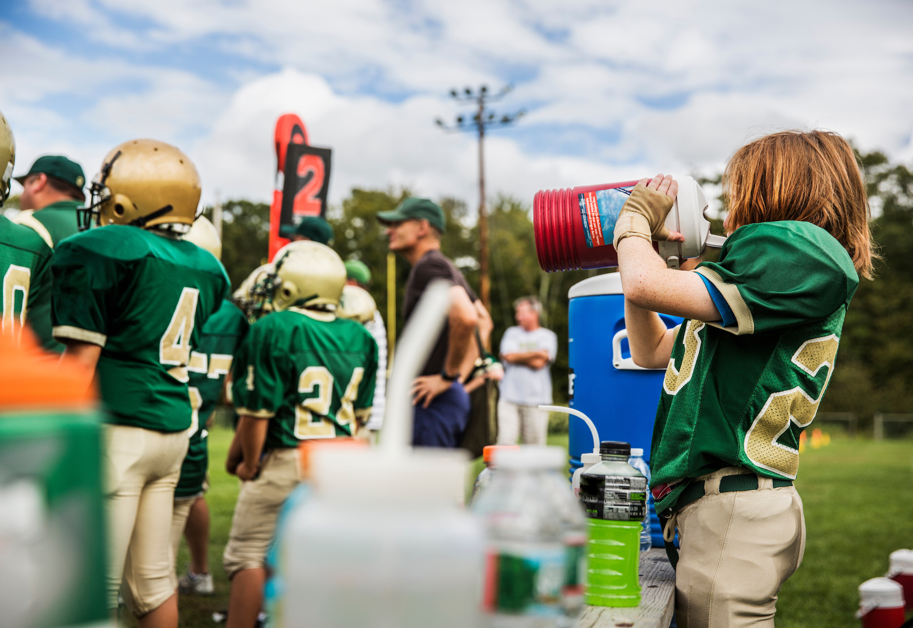 football players standing on a football field with one of them drinking water out of a jug 